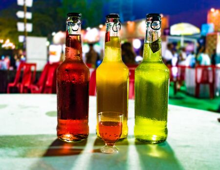 Beautiful photo of Three Wine Bottles placed adjacent to each other. All bottles are of different colored wines and are sealed with ripcap. A small wine tasting glass is placed in front of the bottlesの写真素材