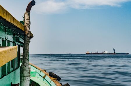 Amazing view from cabin of steamer boat on the way to fishing in high seas, with clear sky, horizon and blue water of ocean in the background and few big vessels at the anchorage of harborの写真素材