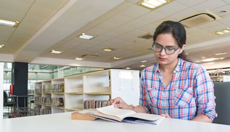 Young intelligent girl in her early 20s, studying in college library and preparing hard for upcoming...