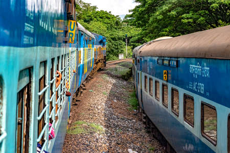 Indian Railways Train departing from station at slow pace, while crossing another train running parallel to it in opposite direction, amidst greenery of Western Ghats.のeditorial素材