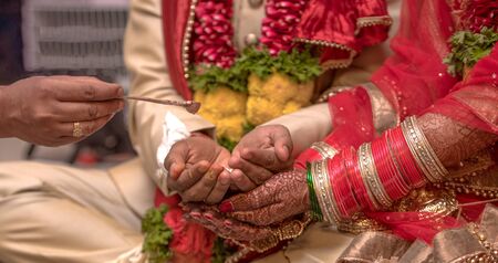 Traditional Indian wedding scene where a beautiful couple is taking part in Hindu rituals of their marriage ceremony. Bride has wore colorful nuptial bangles, while the couple is receiving holy waterの写真素材