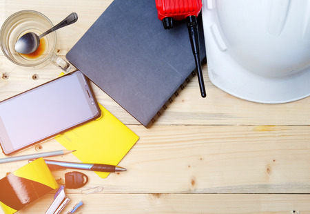 Work desk, construction area with notebook,phone,pen,head protection,radio and coffee cupの写真素材