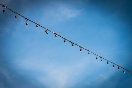 Closeup of the hanging light bulbs with blue sky backgroundの写真素材