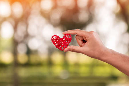 Woman hand holding a red heart on bokeh background on sunlight in the public park, for give...