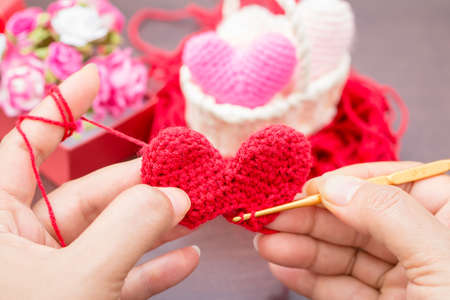 The woman is knitting red heart-shaped with yarn as art crafts to give someone love in the public...