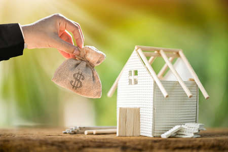 Business man hand hold money bag presenting and home model and wrench and construction tools with repairing put on the wood in the public park,  Loan for business investment of real estate concept.の写真素材