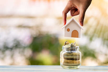 Woman hand hold a wooden home model put on the bottle with gold coin with growing value in the...