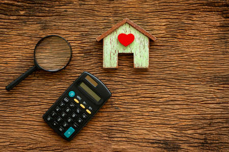 Home model with red heart and calculator and magnifier with searching put on the vintage wood background, Loan for real estate or saving money for buy a new house to family in the future concept.の写真素材