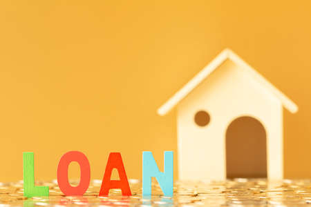 Wooden alphabet loan and home model put on the stacking gold coins in the office, Saving money for buy a new house and plan business investment of real estate concept.の写真素材