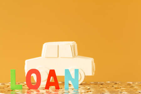 Wooden alphabet loan and car model put on the stacking gold coins in the office, Loan money for buy a new car and a chattel concept.の写真素材