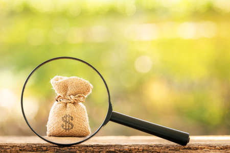 Magnifying glass with searching for money bag put on the wood on bokeh background, Loan and find for...