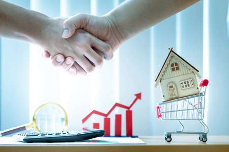 Businessman handshake and home model put in the shopping cart and red bar graph with growing value ...