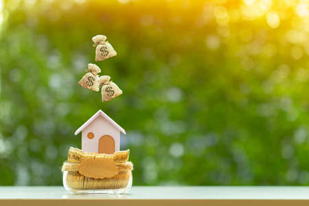 Home model and dropping money bag on the top put on the bottle bank with gold coin in the public...