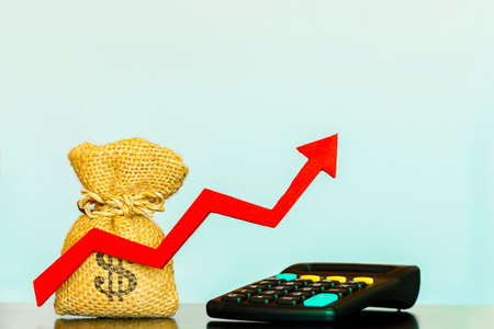 Money bag and red arrow with growing value and calculator put on the desk in the office, for...