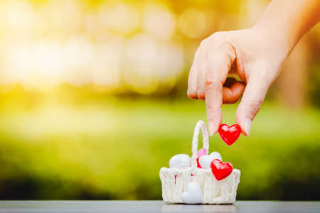 Woman hand holding a red heart put in basket as full heart put on the wood on sunlight in the public...