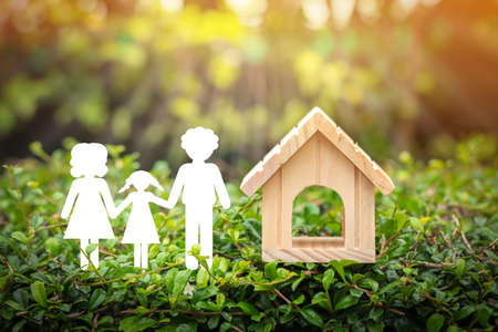A family with paper art and wooden home model put on the grass on sunlight in the public park, The saving money for house or real estate owner in the future concept.の写真素材
