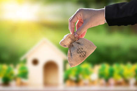 Businessman hand hold a money bag on home model background, Saving money for buy a new house or loan for plan business investment of real estate concept.の写真素材