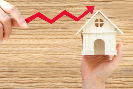 Investor hand holding a home model and a red arrow graph with value increase on the wooden vintage...