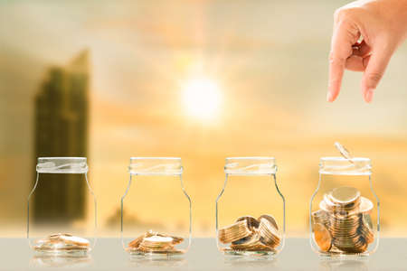 Hands of investors with saves a coin in the bottle bank with growing on photo blur cityscape on...