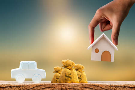 Woman hand hold for select a home model and money bag and car on the wood on sunlight, Loan for...