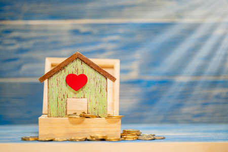 Home model put on the gold coin in the wooden box with grow interest and value on the vintage blue background, Saving money for buy house or loan for plan business investment of real estate concept.の写真素材