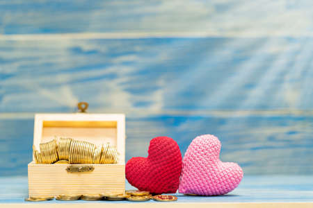 Red and pink heart is made with yarn and gold coin in the wooden box on the vintage blue background,...