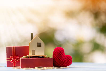 Home model put on the gold coin in the gift box and red heart on sunlight in the public park, The buying a new real estate as a gift to  family or the one loved concept.の写真素材
