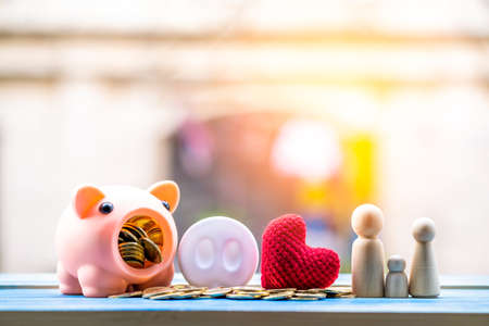 Stacking coins and piggy bank and wooden family and red heart put on the wood on the morning sunlight in public park, Saving money and loan for business investment concept.の写真素材