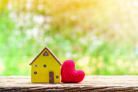 Yellow house model and red heart put on the wood on sunlight in the public park, The buying a new real estate as a gift to family or the one loved concept.の写真素材