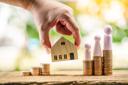 Man hand hold home model for select or give to wood family and stack coin with growing in the public...