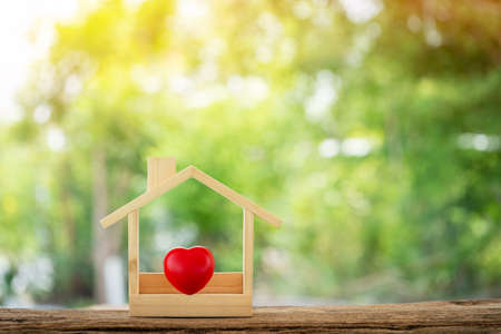 The buying a new real estate as a gift to family or the one loved concept, Red heart placed in the wooden house model put on the old wood on sunlight in the public park.の写真素材