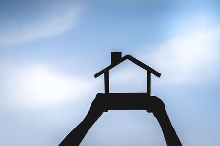 Silhouette of a woman hand holding a home model on blue sky background, The buying a new real estate as a gift to family or the one loved concept.の写真素材