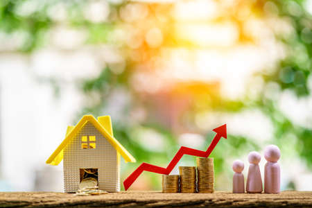 Home model and wooden family and coin with red arrow graph with growing value put on the wood in the public park, The saving money for house or business real estate owner in the future concept.の写真素材