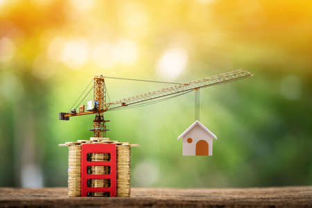 Stacked gold coins with growing and red stairs and tower crane and hoist brake solutions with build new house in the public park, saving money and loan for construction real estate and home concept.の写真素材