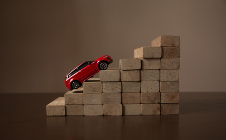 Car goal concept, red car up on roll stair step of wooden staircase stack, natural bright light backgroundの写真素材