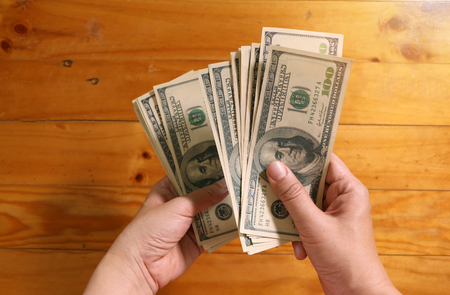 Woman holding  USA dollar money banknotes, top view of female hands with  stack of american cash on wooden tableの写真素材