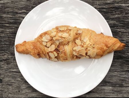 Croissant Almond, a white dish on an old wooden table, ready to eat.の写真素材
