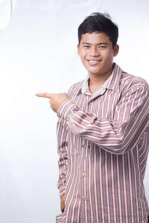 An Asian man is standing with his finger pointing to the right. Behind him is a white background