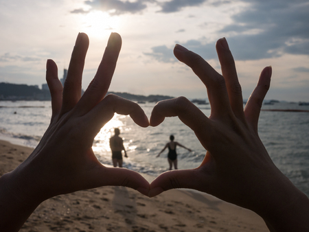 heart shape hand and couple inside on the beach on sunsetの写真素材