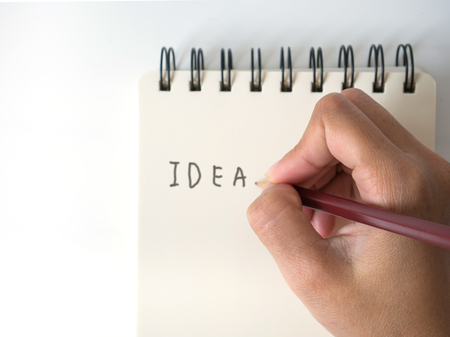 Asian female hand with pencil writing on yellow notebook isolated on white backgroundの写真素材