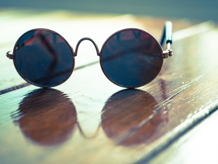 Mini sunglasses on glosy wooden table with reflection: cross processの写真素材