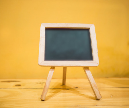 Tripod blackboard on table in yellow background with spaceの写真素材
