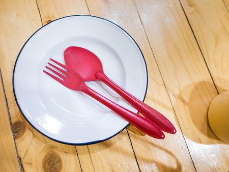 stainless white dish with red folk and spoon on wooden table backgroundの写真素材