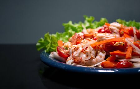 Spicy shrimp salad on dark blue dish with green vegetable in background 