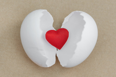 Small red heart hatched from a white egg on a brown backgroundの写真素材