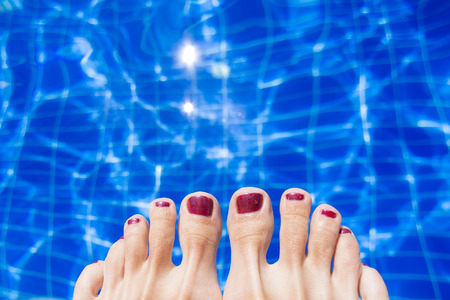 Female feet with red nail polish near the edge of the pool