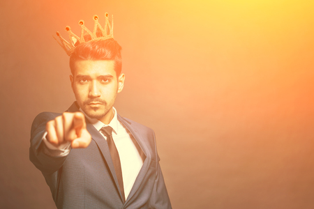 Young attractive man in a blue suit with a crown on his head shows a finger forward in the sunlightの写真素材