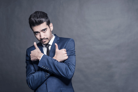 Young attractive man in a blue suit  showing thumb up on a gray backgroundの写真素材