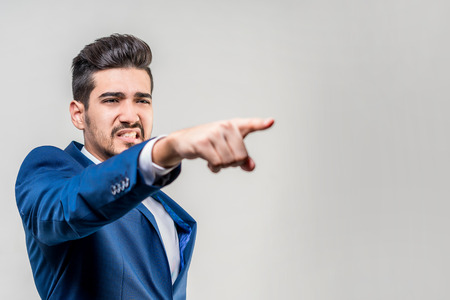 Young attractive man in a blue suit showing a finger forward on a gray background. Isolatedの写真素材