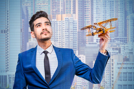 Young attractive man in a blue suit holding a yellow model airplane on the background of skyscrapers